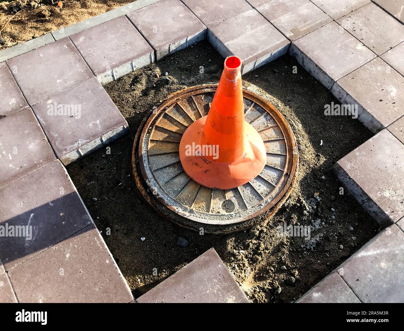 un cono arancione si trova su un tratto pericoloso della strada. il marchio di identificazione in un colore chiaro e distintivo si trova in un foro della strada. la roa Foto Stock