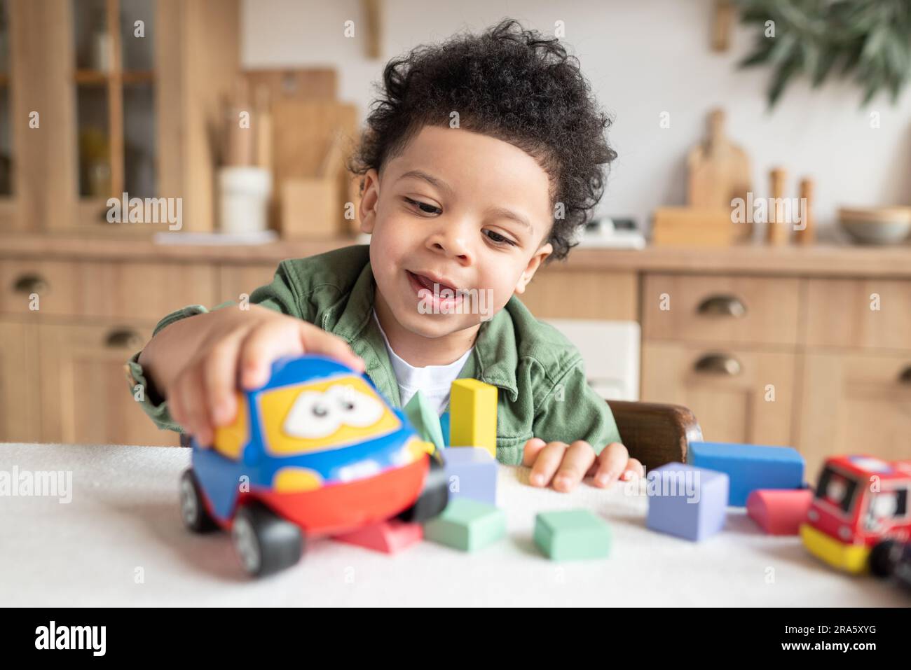 Felice bambino afro-americano con i capelli ricci che giocano con blocchi di legno colorati, che si divertono a giocare da solo nella cucina di casa Foto Stock
