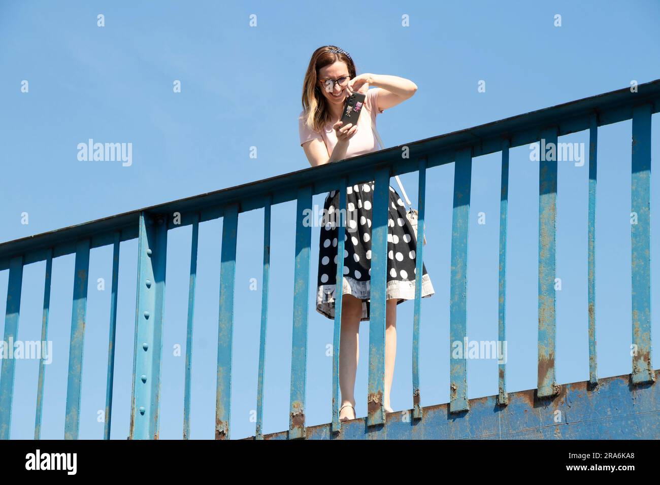 Belgrado, Serbia - 16 giugno 2022: Una donna che scatta fotografie con il cellulare mentre si trova su un ponte, in un giorno d'estate, con un angolo di visione basso Foto Stock