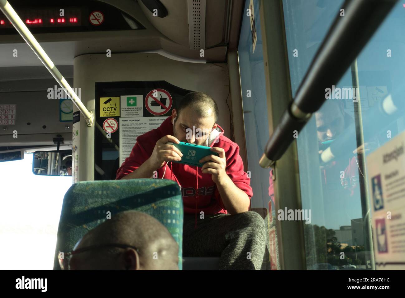 Giovane seduto su un autobus pubblico e giocando con i videogiochi, la Valletta, Malta Foto Stock