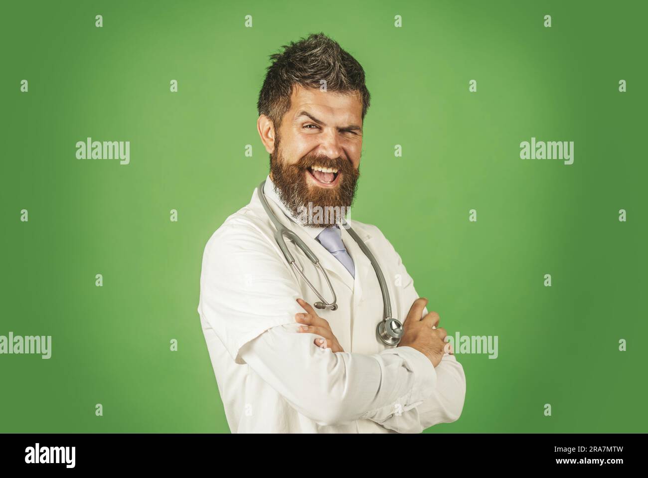 Buon medico in abito medico con stetoscopio sul collo. Medico maschio in abito medico bianco con braccia piegate. Medico sorridente in abbigliamento da lavoro con croce Foto Stock