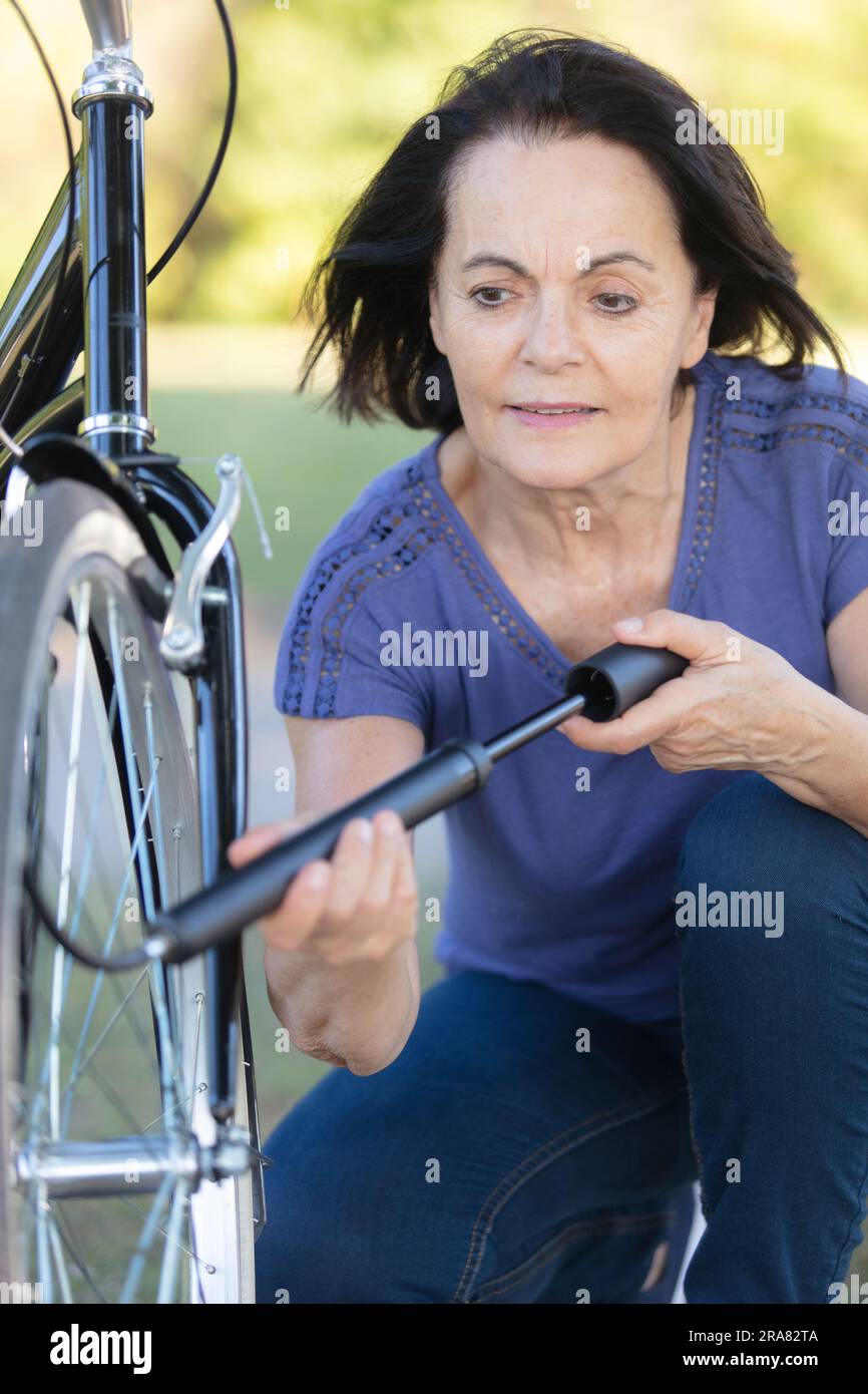 donna anziana che pompa aria in un passo forato attraverso il pneumatico di bicicletta Foto Stock