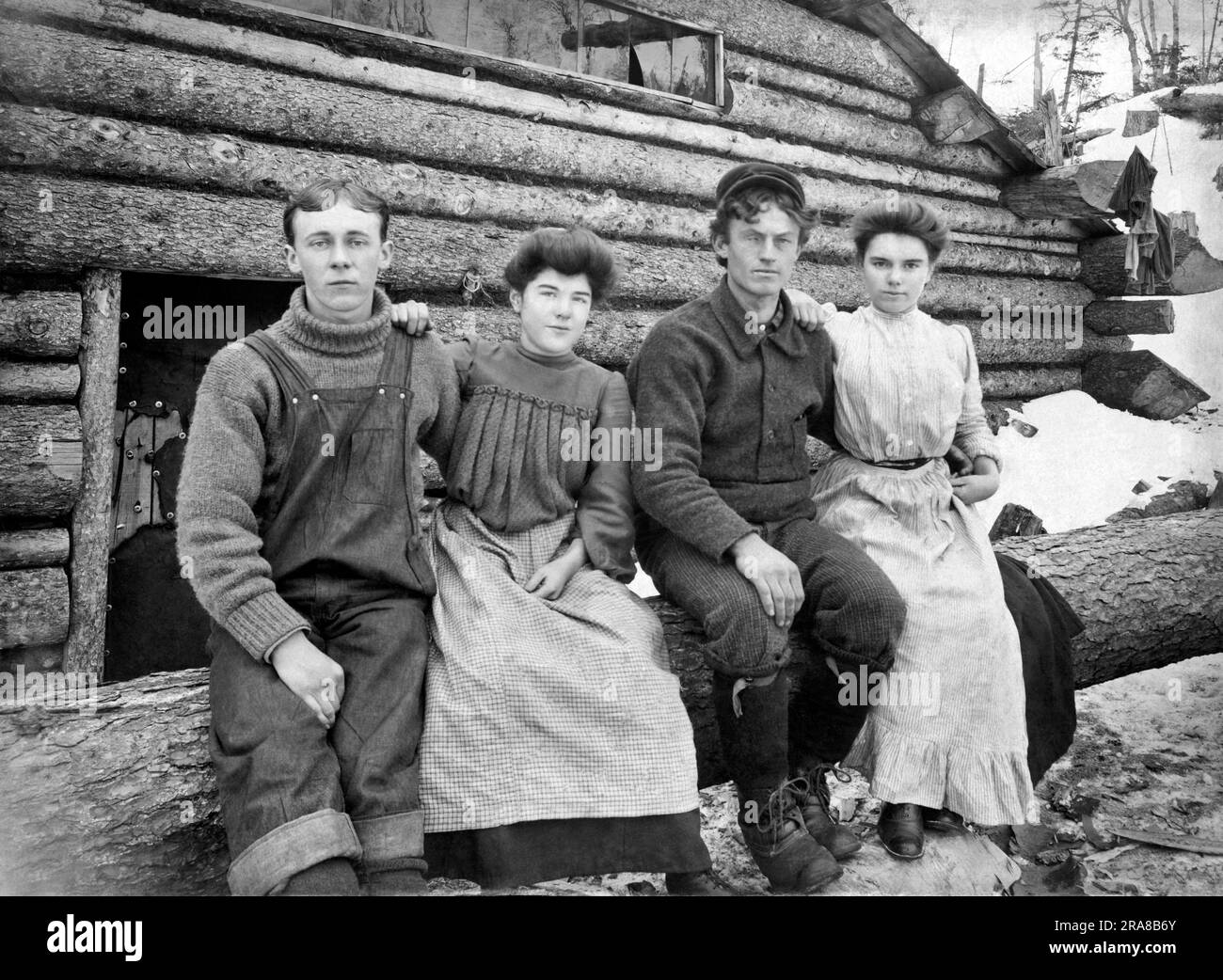 Stati Uniti: c. 1885. Due coppie si siedono sedute su un tronco accanto alla loro capanna di legno nel periodo invernale. Foto Stock