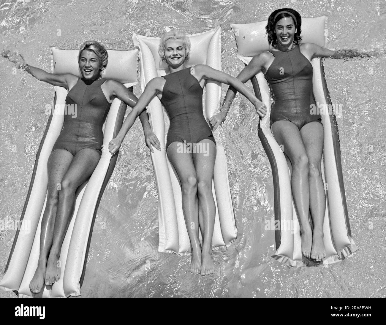Stati Uniti: c. 1962 tre giovani donne in costume da bagno a pezzo unico che galleggiano insieme su zattere in piscina. Foto Stock