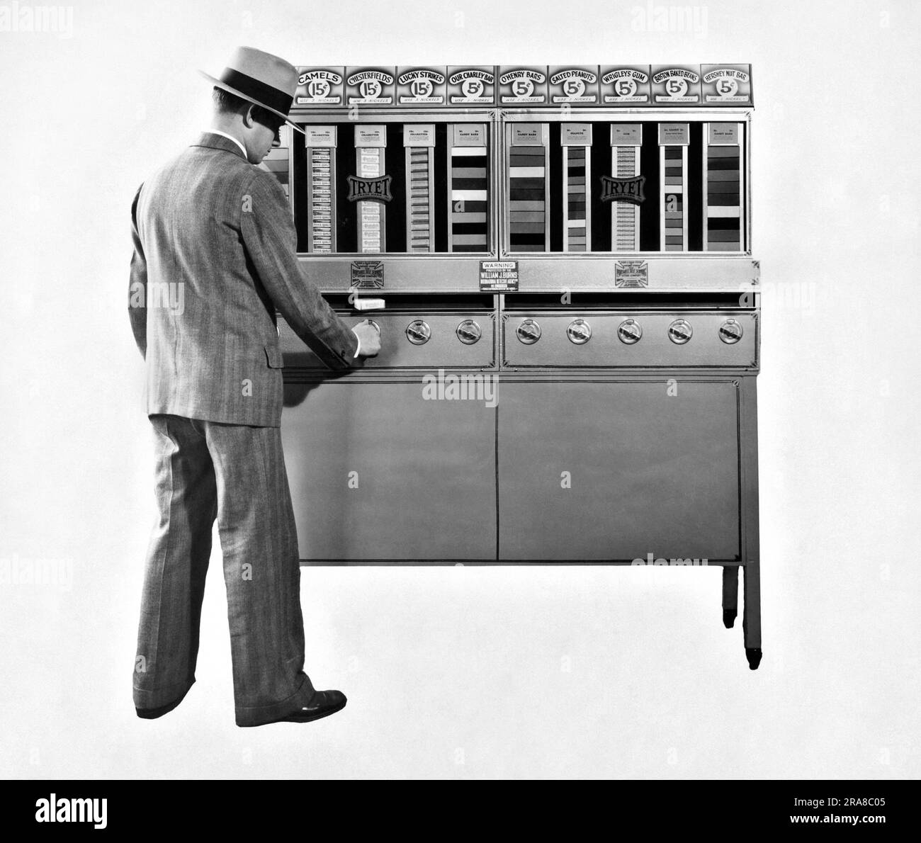 Stati Uniti: c. 1939 Un uomo che acquista un pacchetto di sigarette da un distributore automatico Tryet per sigarette e caramelle. La macchina ha un cartello su di essa che dichiara di essere "protetta dalla William J. Burns International Detective Agency" Foto Stock