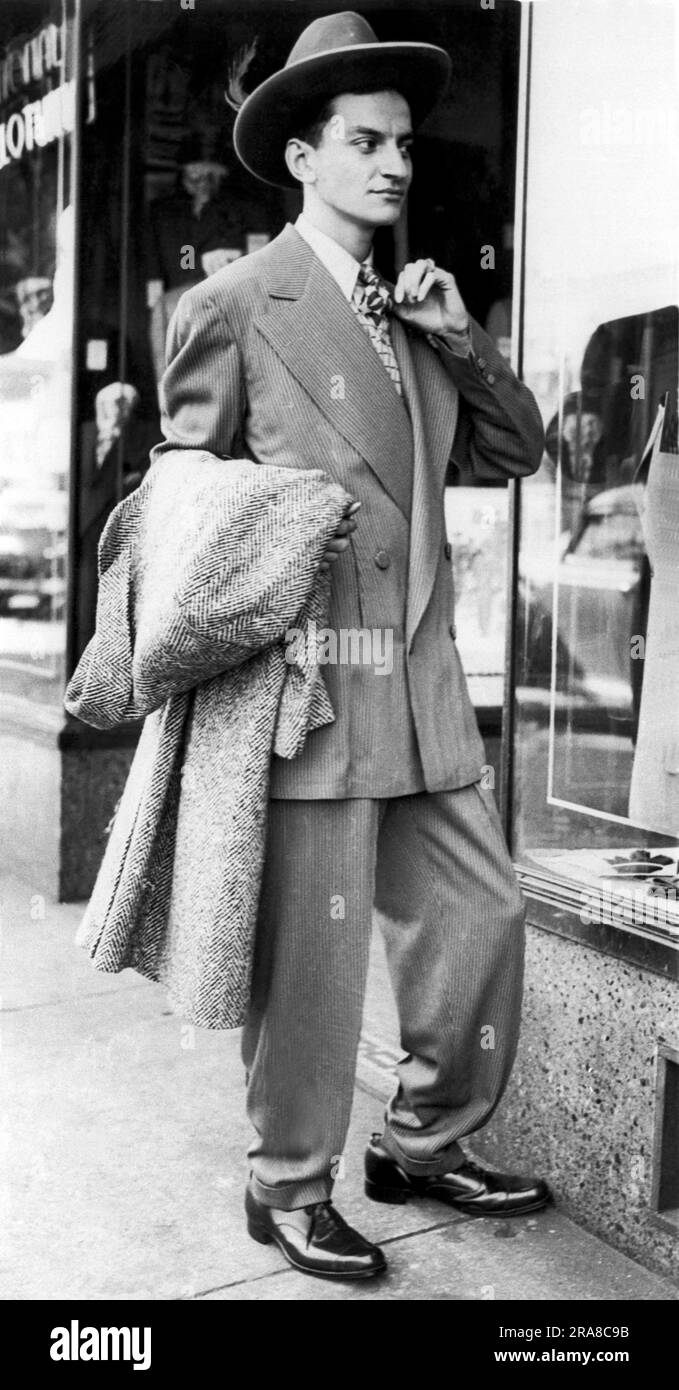 Chicago, Illinois: 1943. Un giovane vestito con una tuta zoot controlla la sua immagine in una vetrina del negozio. Questo è stato in qualche modo modificato per conformarsi alle regole del tempo di guerra per preservare il tessuto. Foto Stock