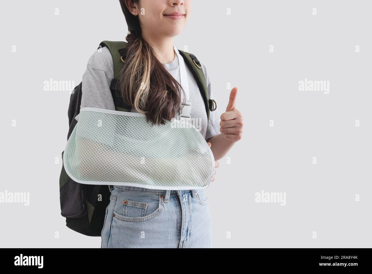 Concetti di assicurazione di viaggio. Giovane donna con la mano ferita con scheggia, braccio rotto, zaino, pollice in alto, faccia sorridente Foto Stock