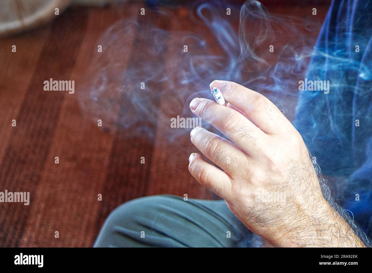Mano di un uomo che fuma una sigaretta, producendo fumo e danni alla salute Foto Stock