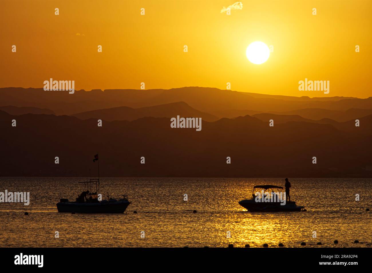 Paesaggio idilliaco con barche galleggianti sull'acqua dorata del mare e sulle montagne al tramonto Foto Stock