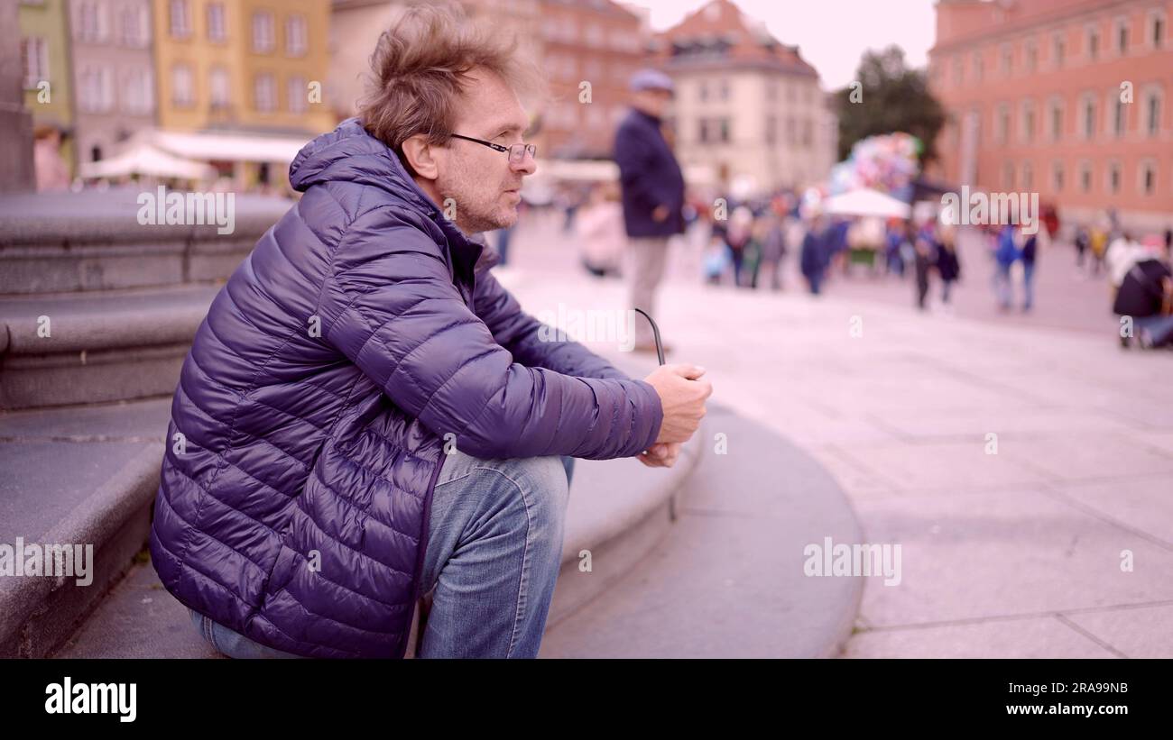 Uomo adulto seduto sulla piazza e fumando una canottina di tabacco nella Piazza del Palazzo, nel centro storico di Varsavia Foto Stock