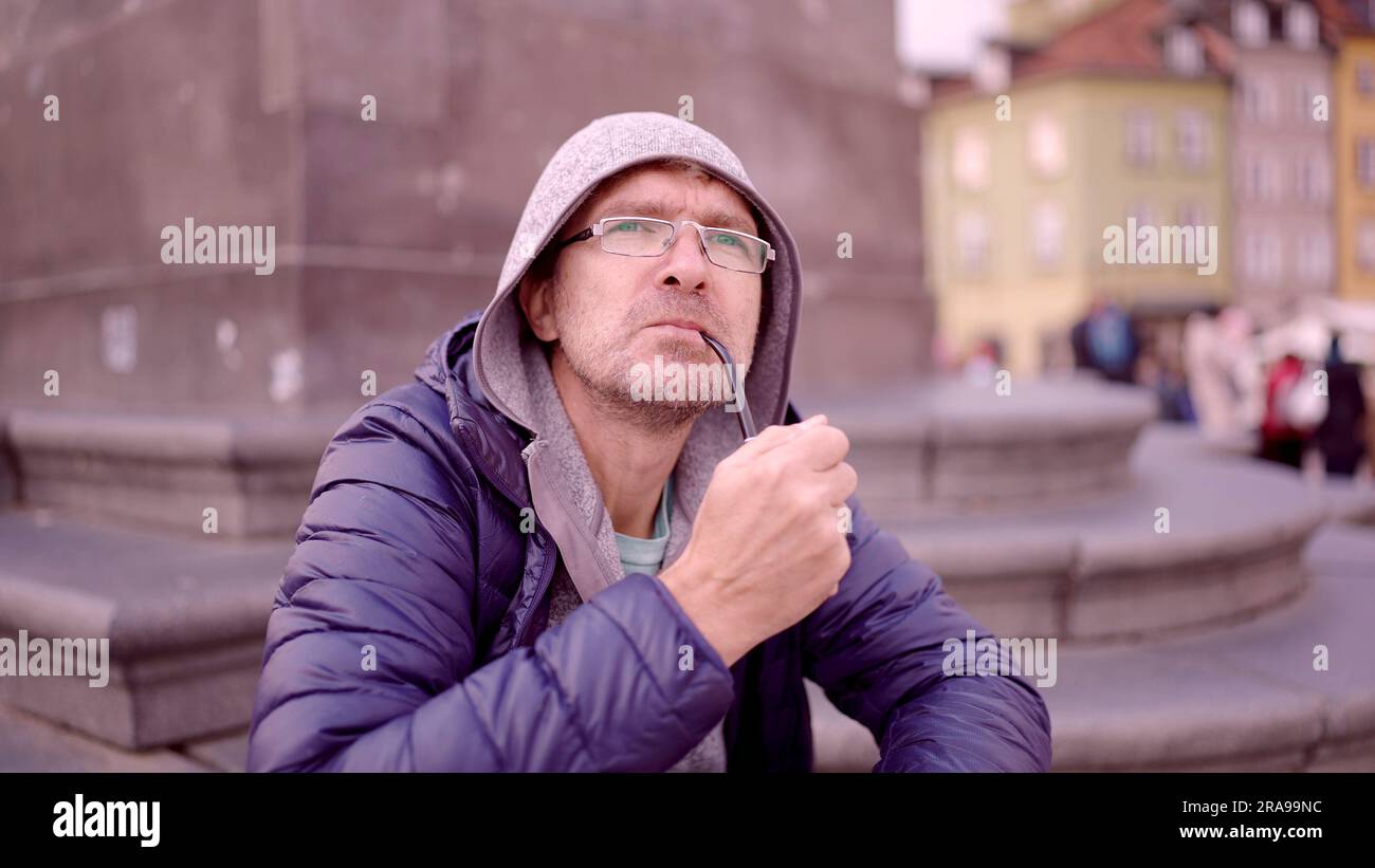Ritratto di un uomo adulto con occhiali seduti nel cappuccio sulla piazza e fumare un tubo di tabacco nella Piazza del Palazzo, nella Città Vecchia di Varsavia Foto Stock