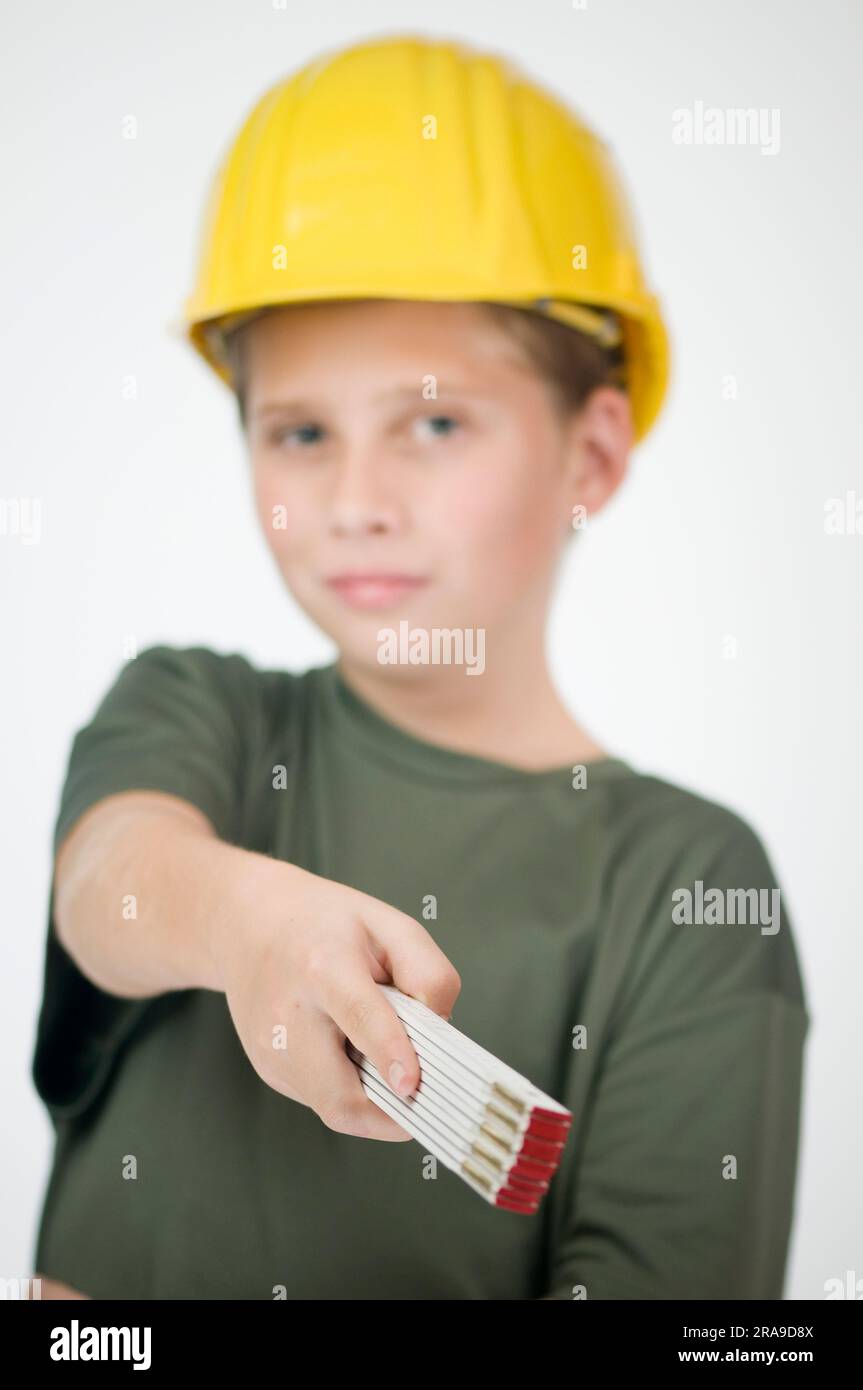 Osserva un giovane adolescente che indossa un casco giallo e tiene un righello pieghevole nella mano destra, puntando verso la fotocamera. Foto Stock