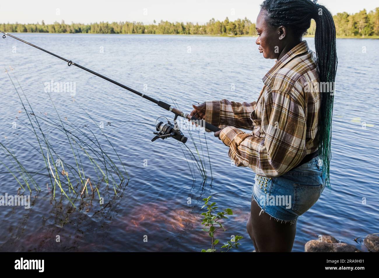 La donna si alza in piedi e si muove in lenza durante una battuta di pesca in uno dei laghi svedesi in una soleggiata giornata estiva. Foto Stock
