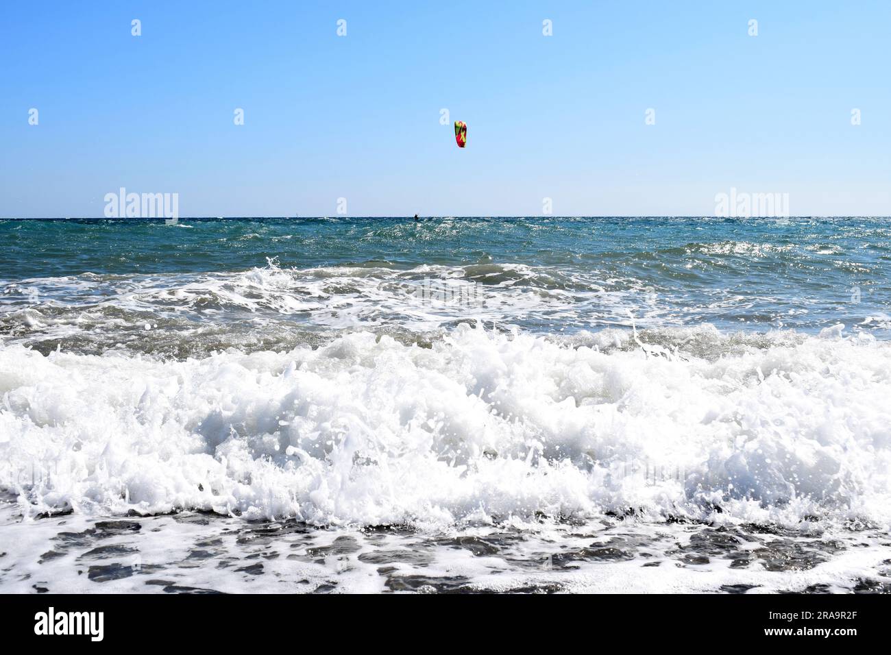 Onde bianche e schiumose con il kite surfer in lontananza in una giornata soleggiata e nuvolosa nel Mar Mediterraneo, Liguria, Italia Foto Stock
