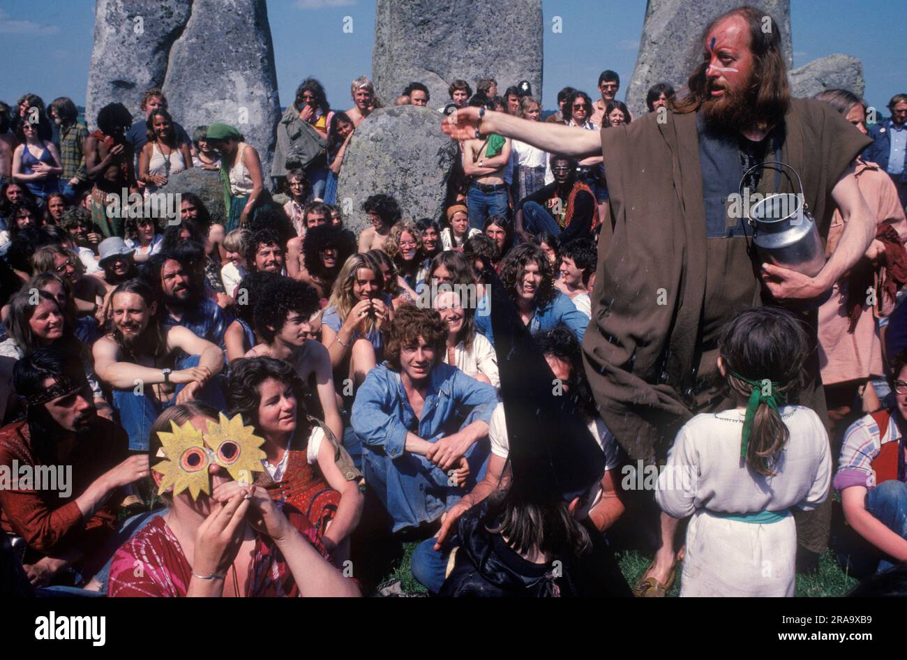 Gli hippy in stile anni '1970 partecipano al festival gratuito di Stonehenge per celebrare il solstizio d'estate. Una donna hippy che indossa una maschera celebra il mitologico Dio del Sole celtico, Belenus. SID Rawle, noto come il re degli hippy, spruzza l'acqua al gruppo come benedizione. Stonehenge Free Festival al solstizio d'estate, Wiltshire, Inghilterra 21 giugno 1979. 70S UK HOMER SYKES Foto Stock