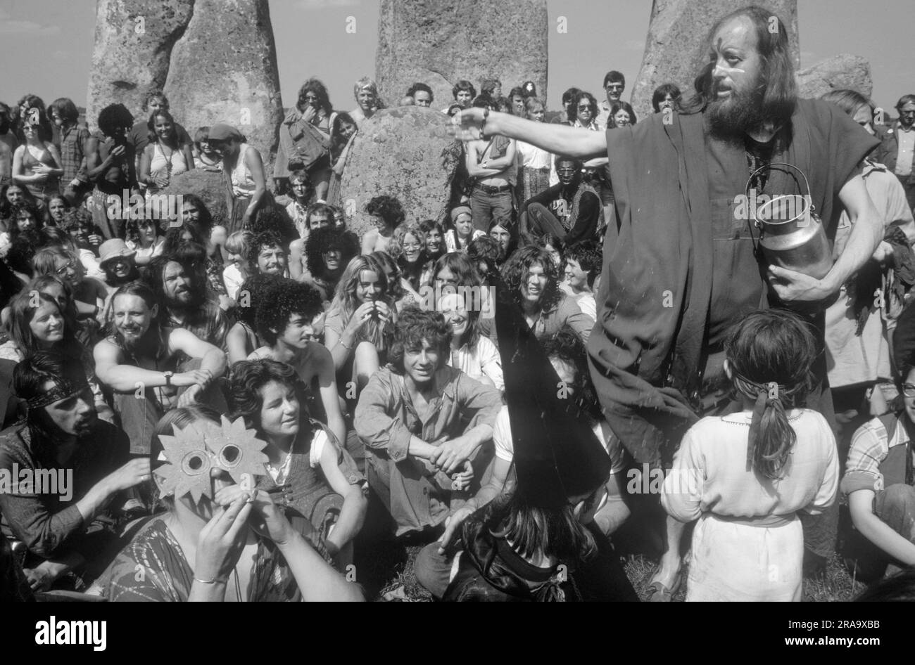 Stonehenge Free Festival al solstizio d'estate, Wiltshire, Inghilterra 21 giugno 1979. Gli hippy in stile anni '1970 partecipano al festival gratuito di Stonehenge per celebrare il solstizio d'estate. Una donna hippy che indossa una maschera celebra il dio del sole Belenus. SID Rawle, noto come il re degli hippy, spruzza l'acqua al gruppo come benedizione. 70S UK HOMER SYKES Foto Stock