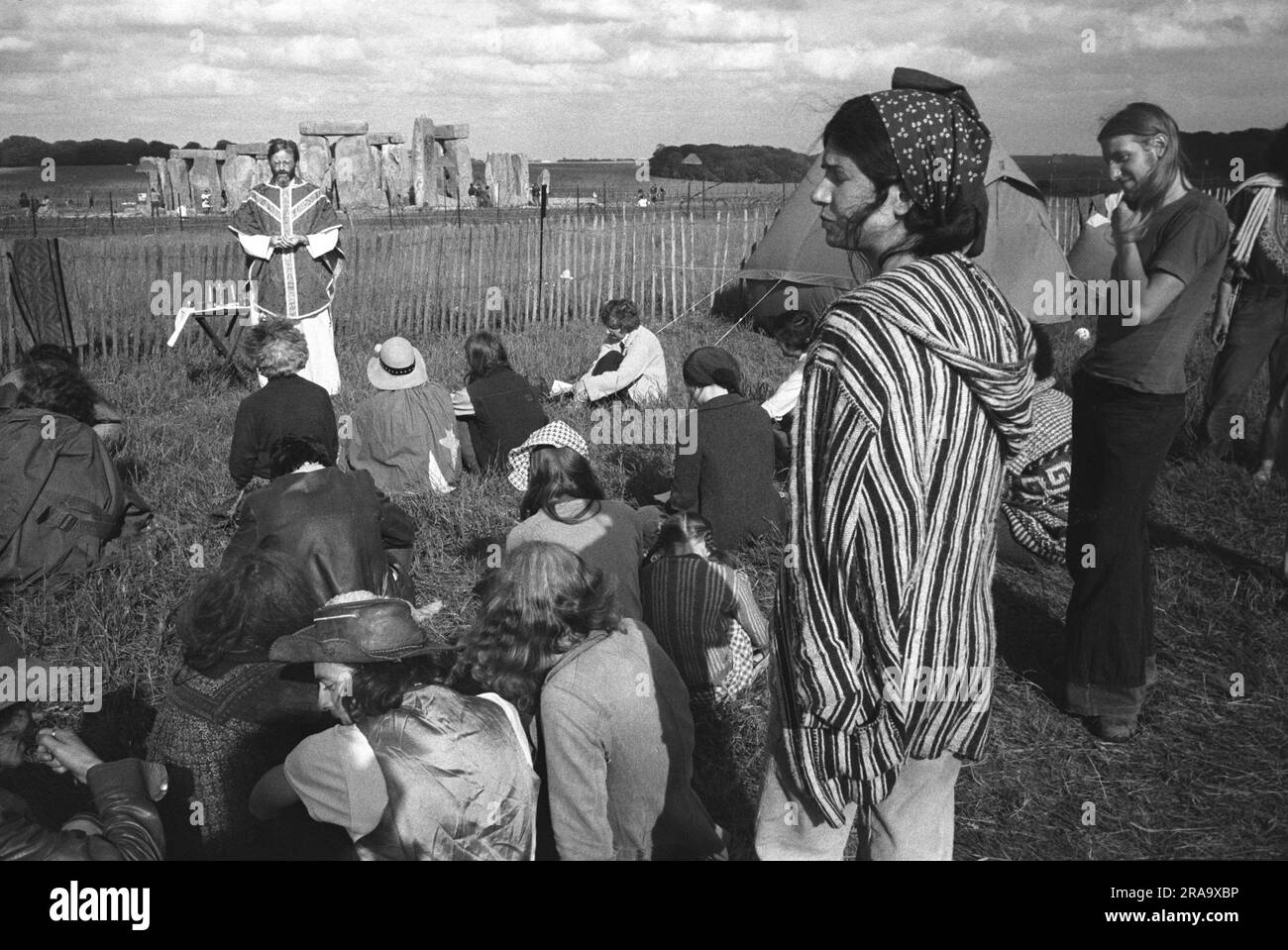 I frequentatori del festival ascoltano un prete che è venuto a tenere una funzione religiosa all'aperto. Stonehenge Free Festival al solstizio d'estate, Wiltshire, Inghilterra, giugno 1976. 1970S UK HOMER SYKES Foto Stock