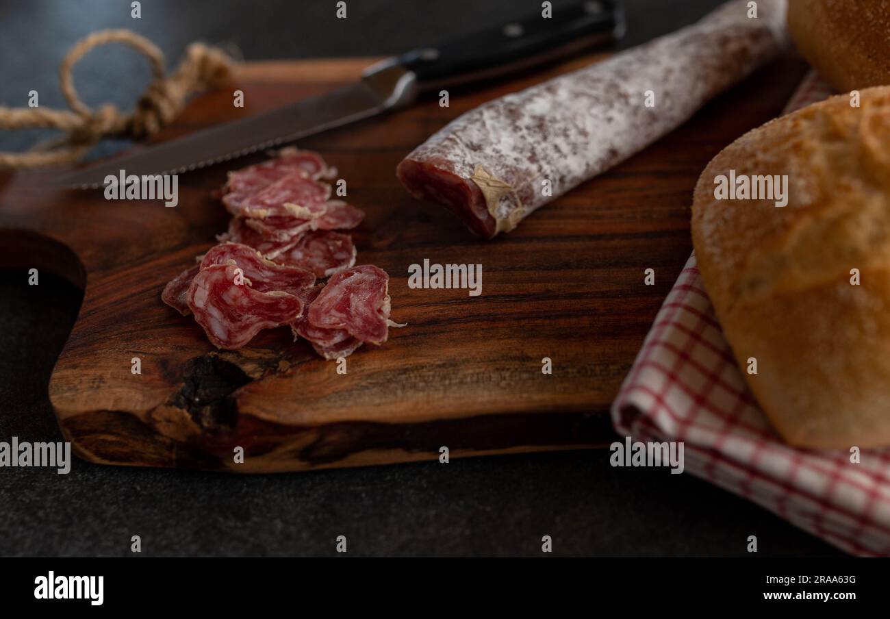 Salame spagnolo a fette, fuetec di maiale iberico su una tavola di legno con coltello Foto Stock
