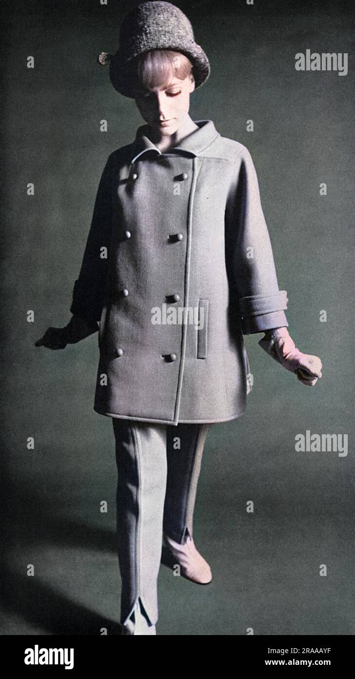 Un vestito di moda Koupy che traduce la silhouette dettata da Courreges sulla passerella parigina. Qui, un tuta da pantaloni in twill di cavalleria blu ardesia comprende una giacca a mezza cintura con una fessura sul retro, indossata con i famosi pantaloni Courreges a doppia cucitura. Il piccolo cappello tweed è del milliner Simone Mirman. Data: 1964 Foto Stock