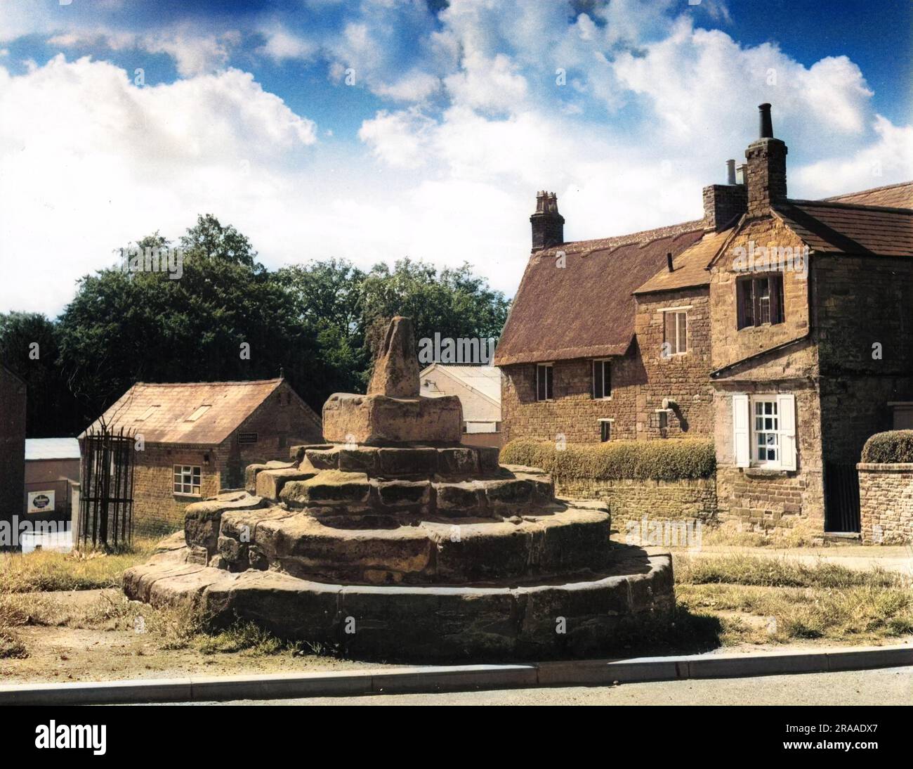 La base dell'antica croce di mercato, posta lungo la strada, nel villaggio di Brixworth, Northamptonshire, Inghilterra. Data: Anni '1950 Foto Stock