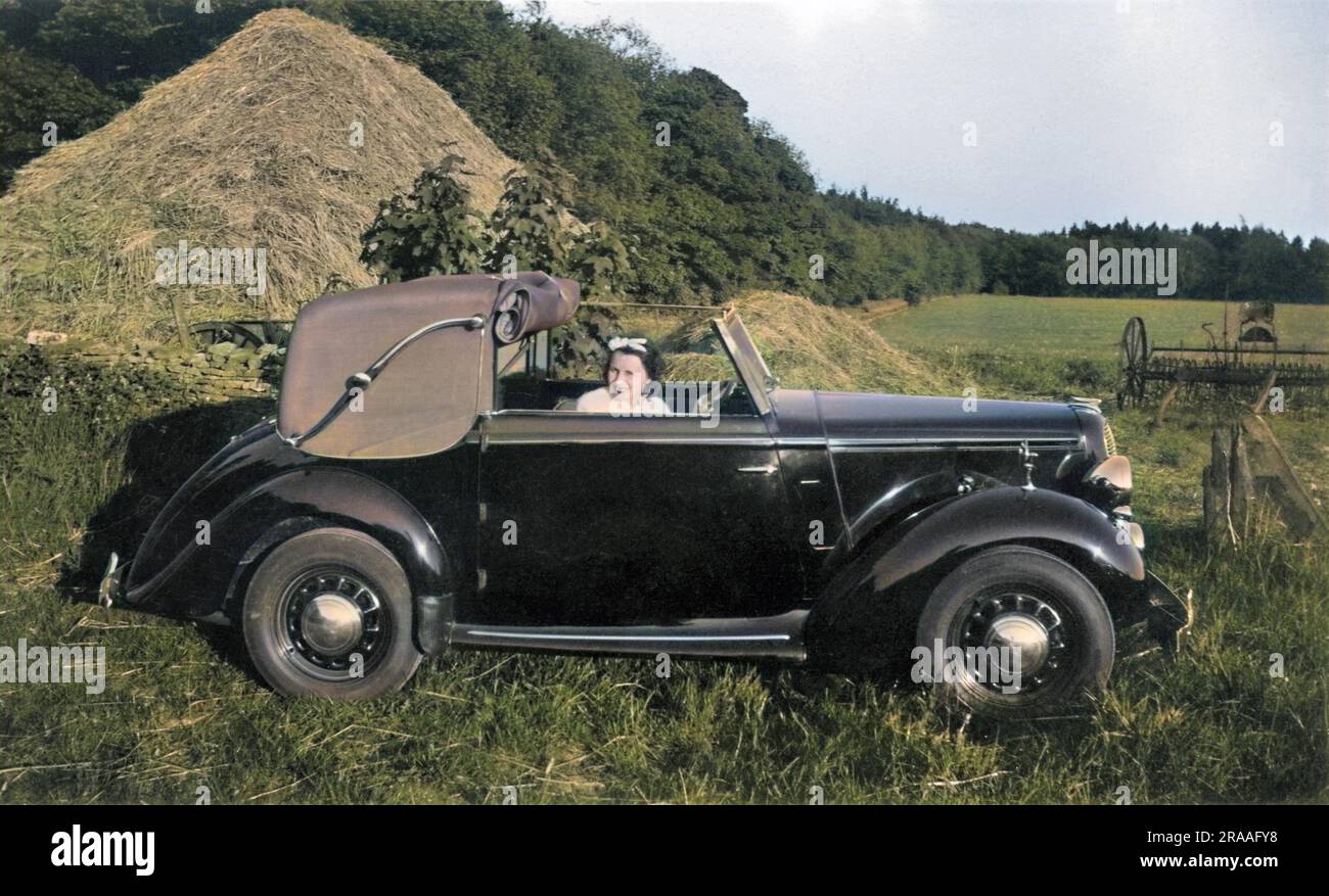 Donna seduta in una macchina in un campo vicino a un pagliaio. Data: 1939 Foto Stock