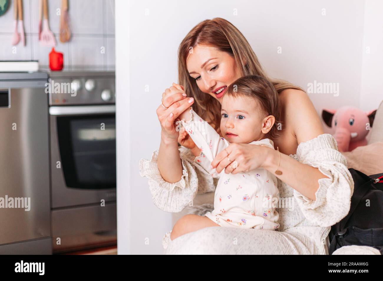 La giovane mamma veste la sua bambina nel loro ambiente domestico Foto Stock