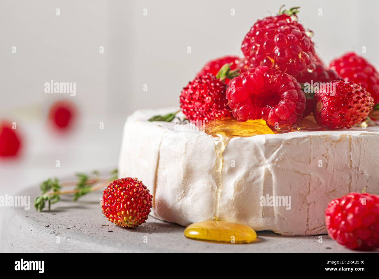 Formaggio Camembert con lamponi freschi, fragole, miele e timo su sfondo bianco. Antipasto francese Foto Stock