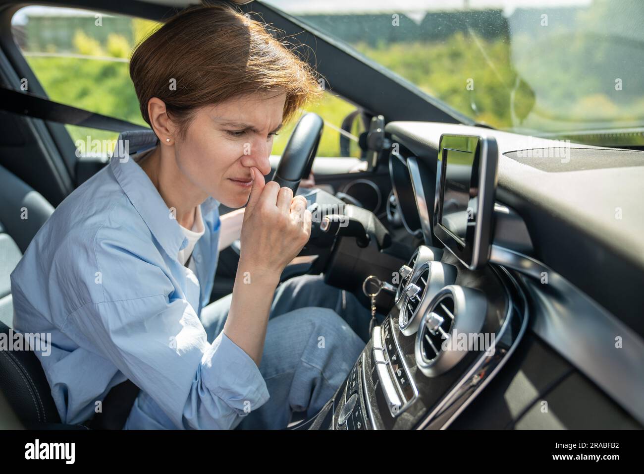 Donna conducente che sente un odore sgradevole proveniente dall'impianto di climatizzazione durante la guida di un'auto con clima caldo. Foto Stock