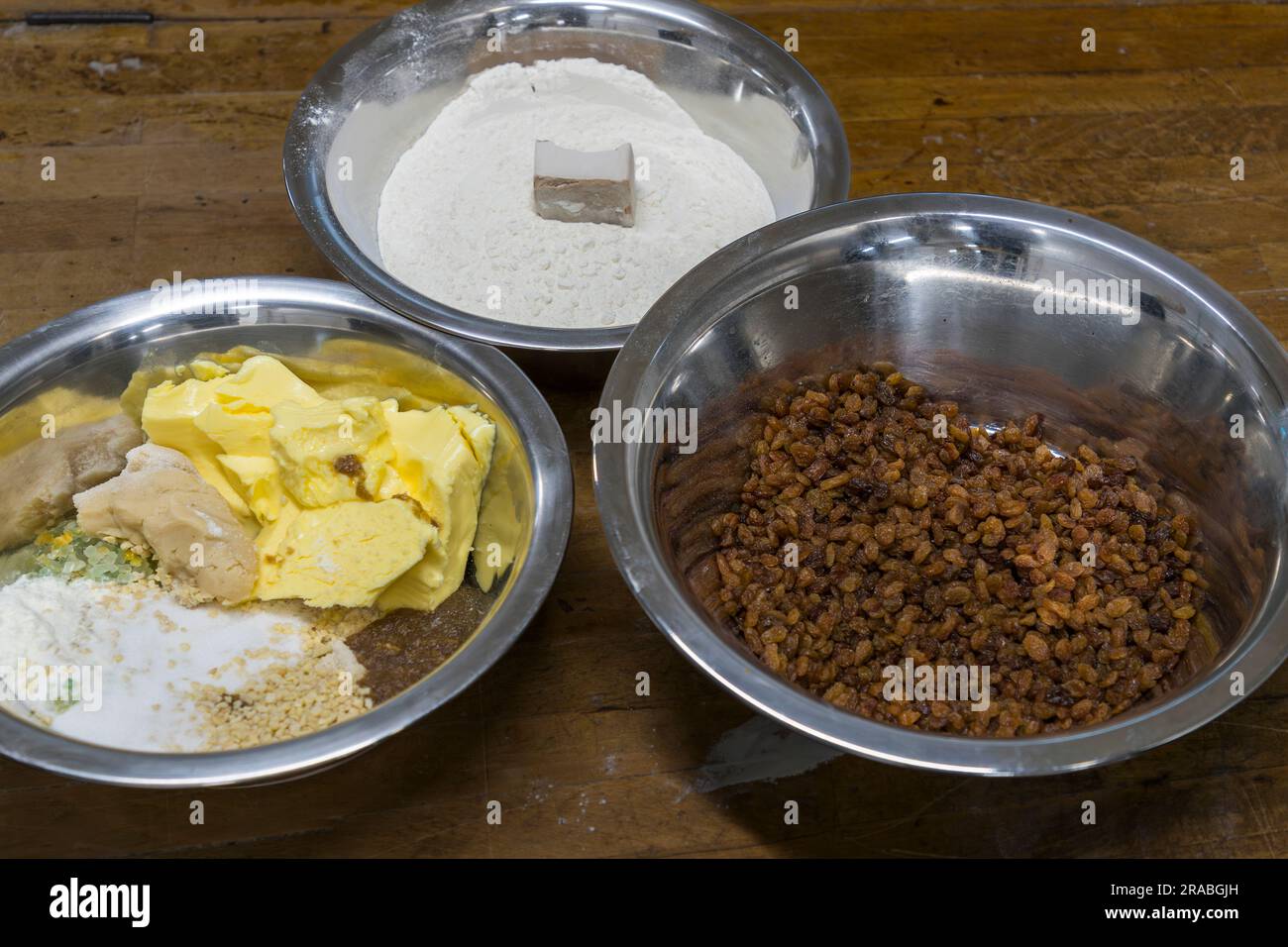 Tre ciotole di ingredienti di base per l'originale Christstollen di Dresda sono disposte su un tavolo di legno: farina con un pezzo di burro, una miscela di burro, pasta di mandorle e spezie e una ciotola di uvetta. Ogni panificatore di Stollen di Dresda ha la sua ricetta, basata sugli ingredienti di base prescritti ma contenente piccoli segreti nelle spezie o nel rapporto esatto di miscelazione. La fotografia è stata scattata nella panetteria Dresdner Backhaus, Dresda, Sassonia, Germania. Foto Stock