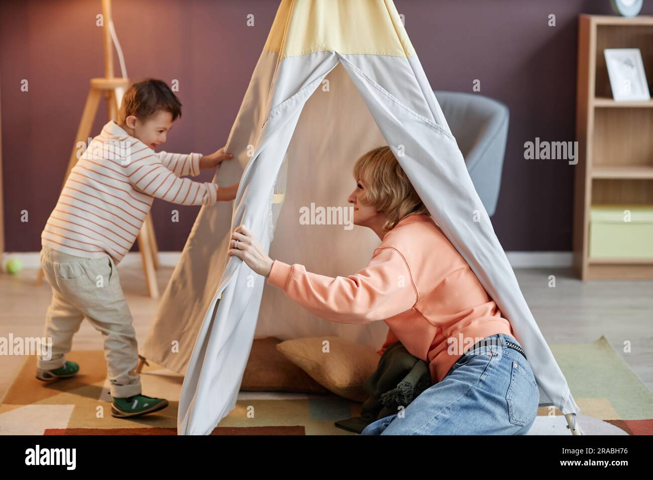 Ritratto completo di bambino con sindrome di Down che gioca con la madre in tenda da da gioco a casa Foto Stock