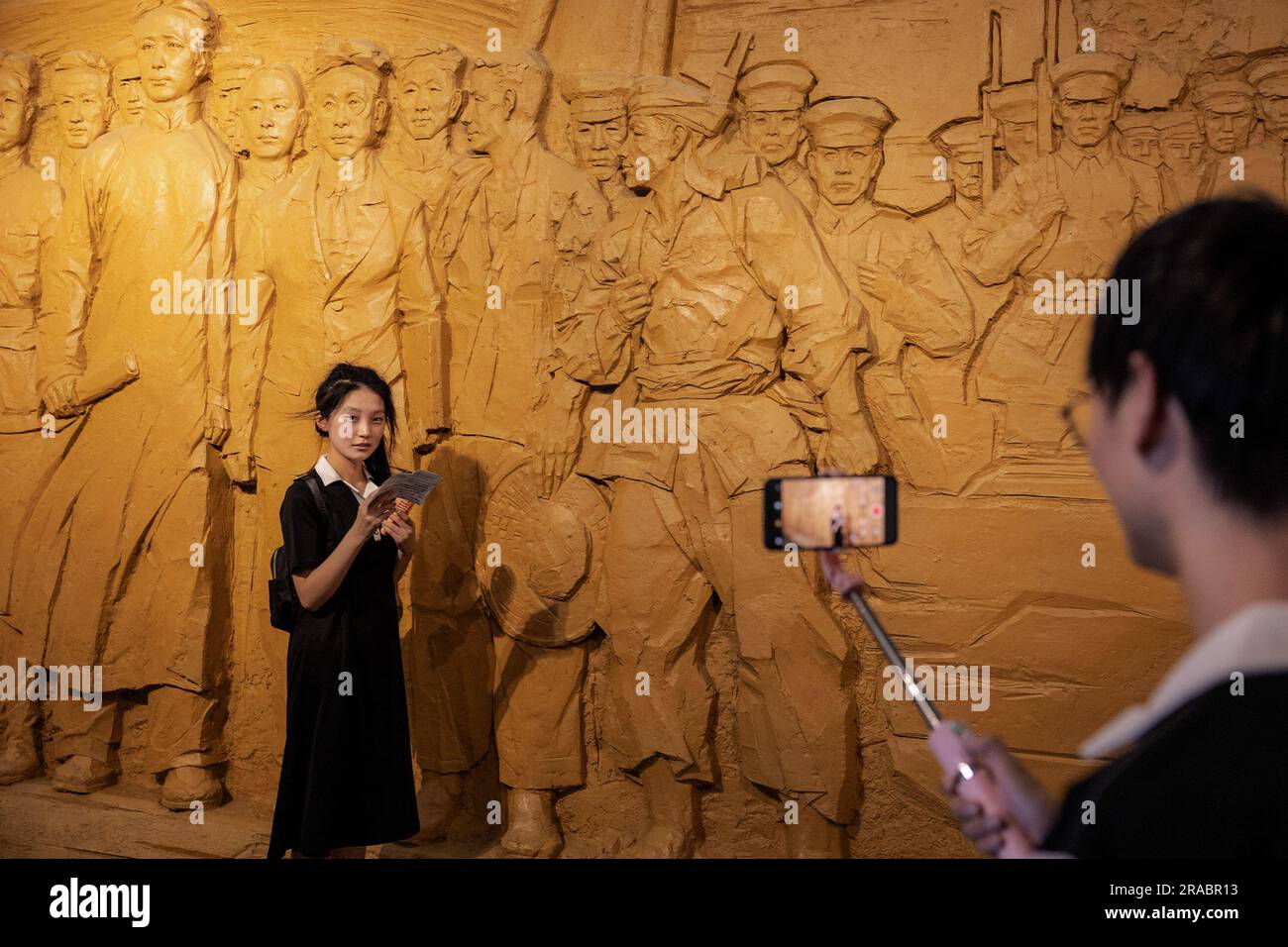 Wuhan, Cina. 1 luglio 2023. Gli studenti universitari registrano un video con telefono davanti a un muro con rilievi di Mao Zedong e soldati al Museo rivoluzionario di Wuhan durante il 102° anniversario della fondazione del Partito Comunista Cinese (PCC) a Wuhan. Prima dell'anniversario della fondazione del PCC, i dati ufficiali hanno rivelato che l'appartenenza al PCC ha segnato un aumento di quasi 1,33 milioni, ovvero il 1,4%, da 2021 a 98,04 milioni alla fine del 2022. Credito: SOPA Images Limited/Alamy Live News Foto Stock