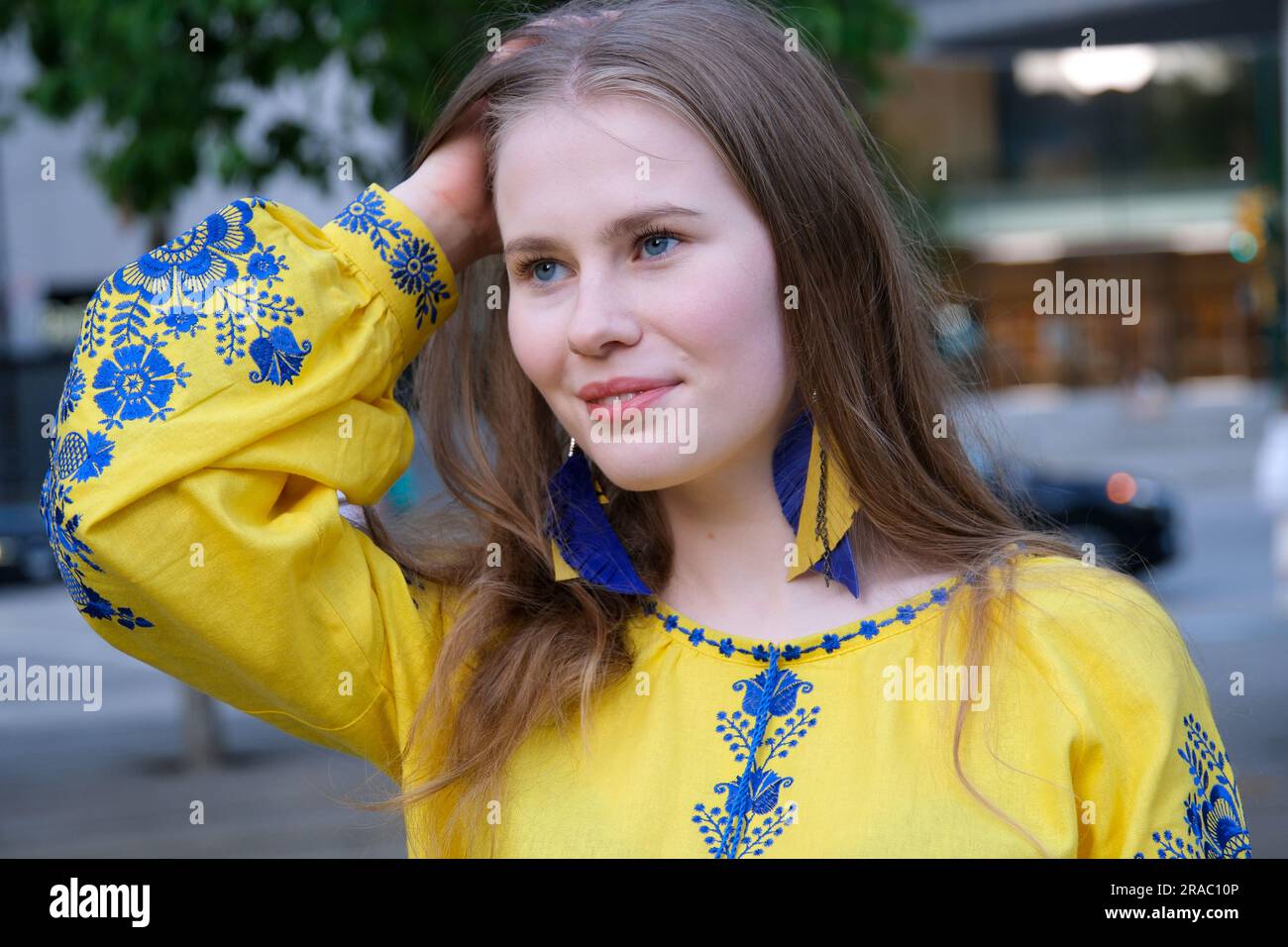 lisciate i capelli con le mani lunghi orecchini pendenti in fiori blu e gialli ricamati. La ragazza indossa una camicia ricamata, abiti nazionali ucraini, una camicia gialla. Foto Stock