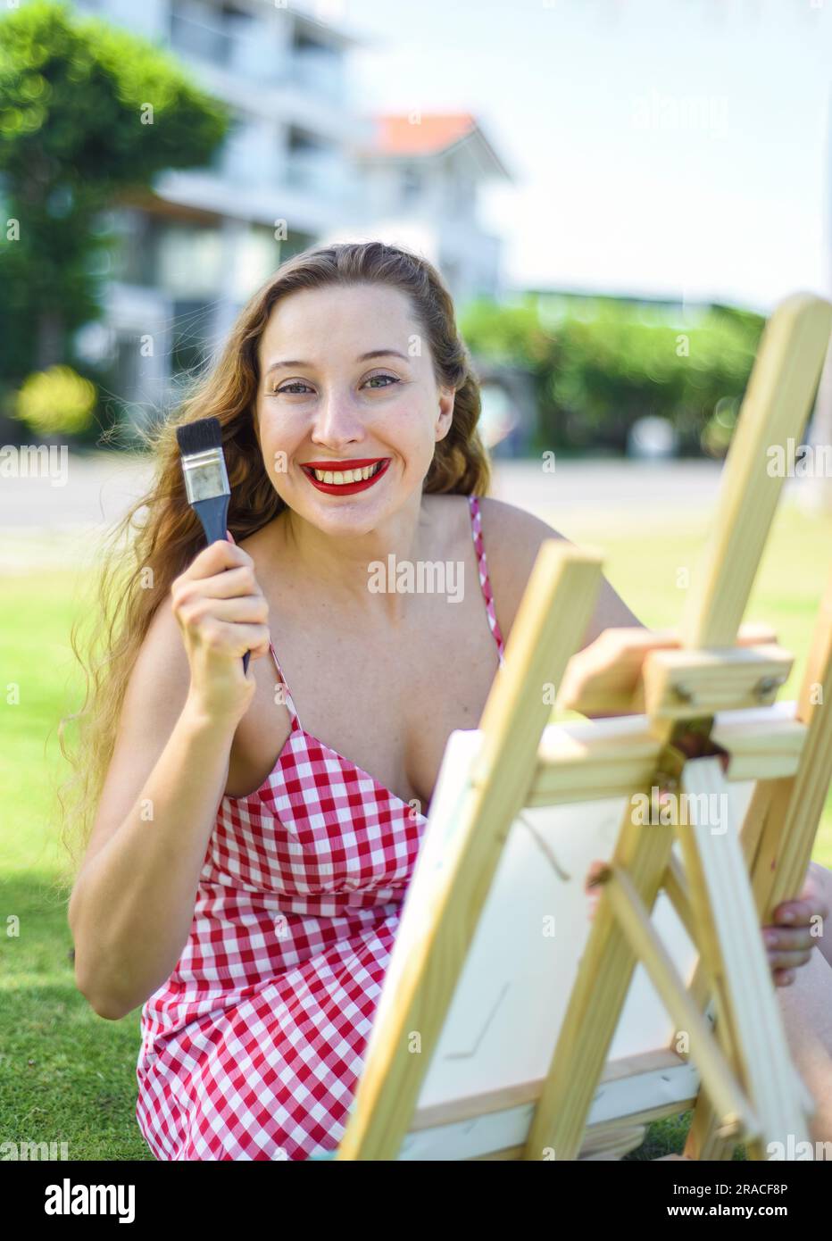 Giovane artista che tiene in mano un barattolo con pennelli e cavalletto vicino al mare e alle palme in estate Foto Stock