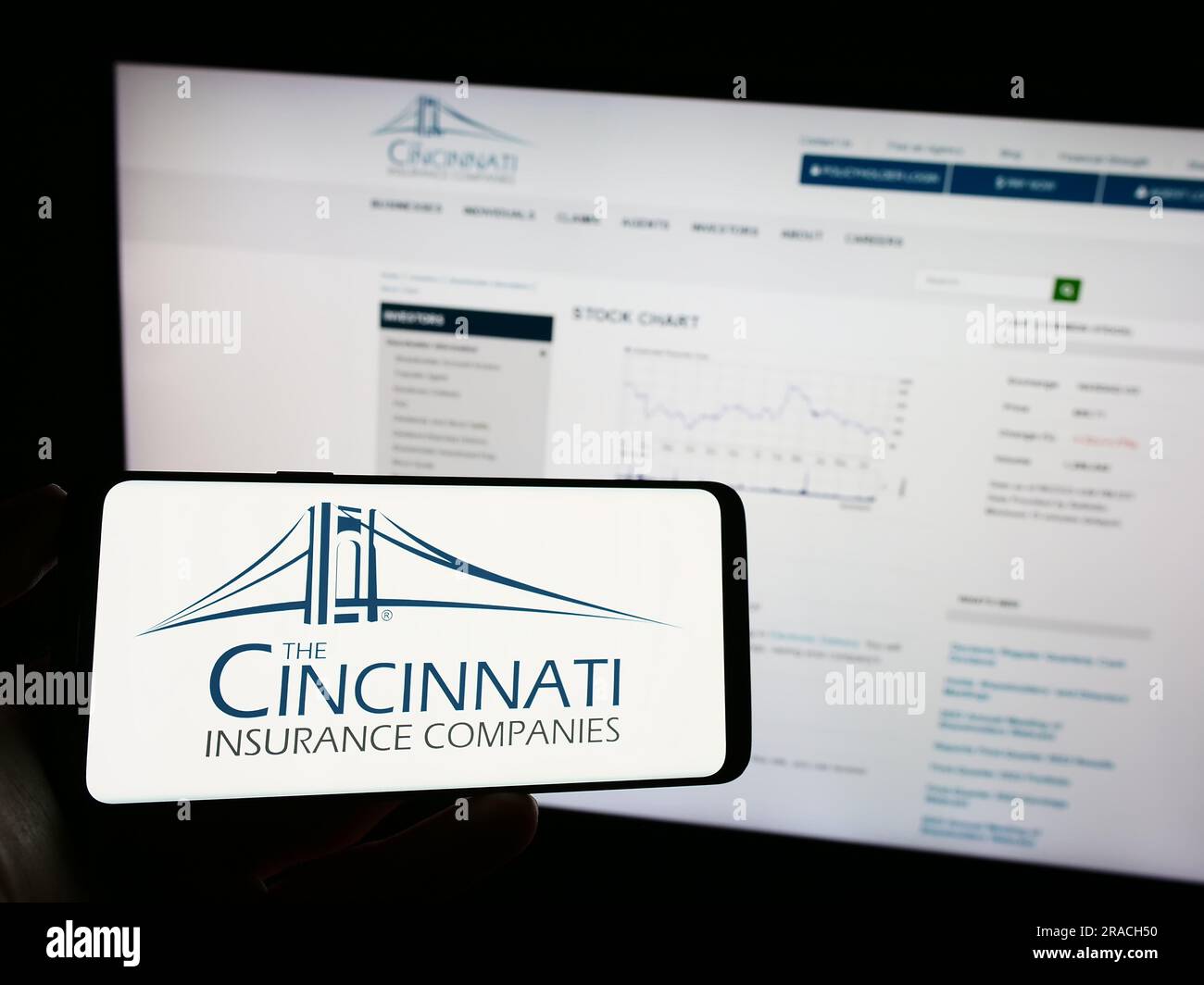 Persona che possiede un telefono cellulare con il logo della società statunitense Cincinnati Financial Corporation sullo schermo davanti alla pagina Web. Concentrarsi sul display del telefono. Foto Stock