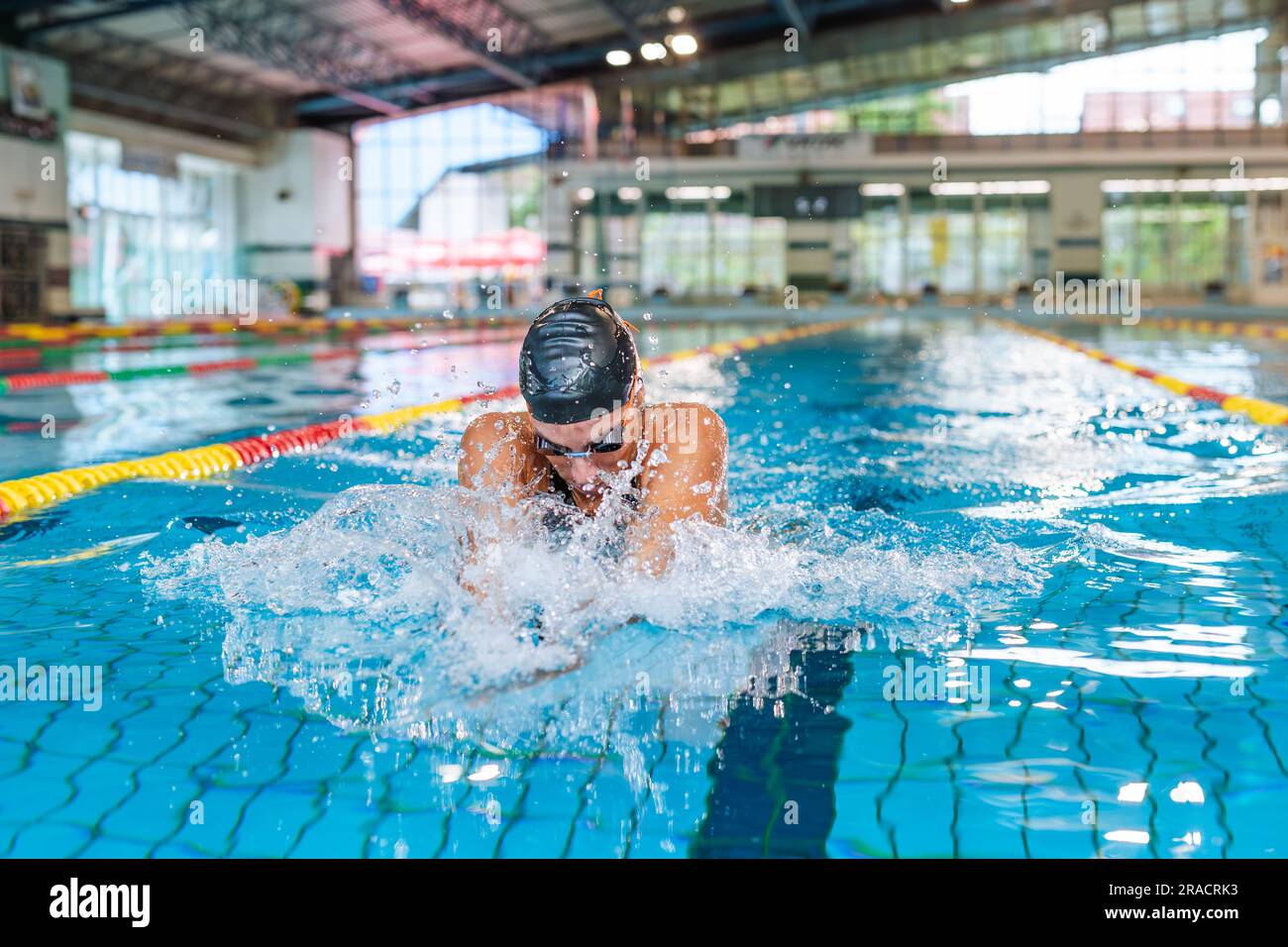 Atleta femminile che nuota in stile senstroke nella corsia della piscina, che si fa strada, si immerge e si solleva dall'acqua per respirare. Foto Stock