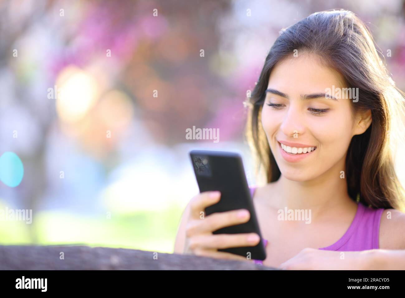 Donna felice che usa uno smartphone in un bellissimo parco viola Foto Stock