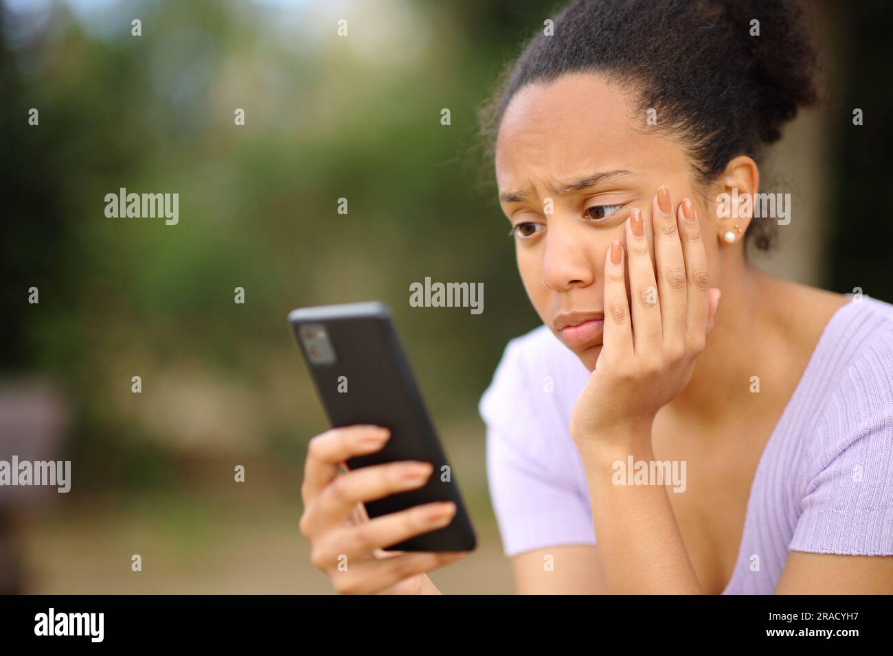 Preoccupata donna nera che controlla il cellulare seduto in un parco Foto Stock