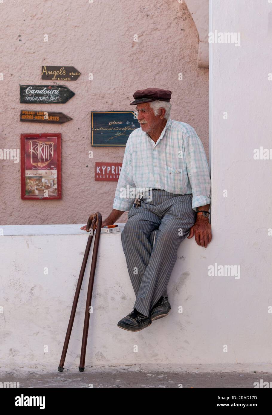Un anziano greco seduto su un muro basso osserva il paesaggio sull'isola di Santorini in Grecia Foto Stock