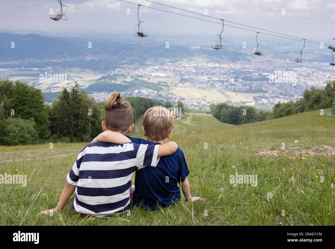 Due ragazzi amici che si abbracciano mentre si siedono in montagna il giorno d'estate, godendosi il panorama. Fratello amore. Concetto di amicizia. Vista posteriore. Attivo Foto Stock
