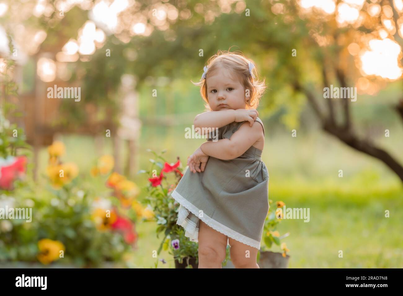 una graziosa bambina con un abito da sole in cotone verde cammina in estate al tramonto in estate a piedi nudi al tramonto. Foto di alta qualità Foto Stock