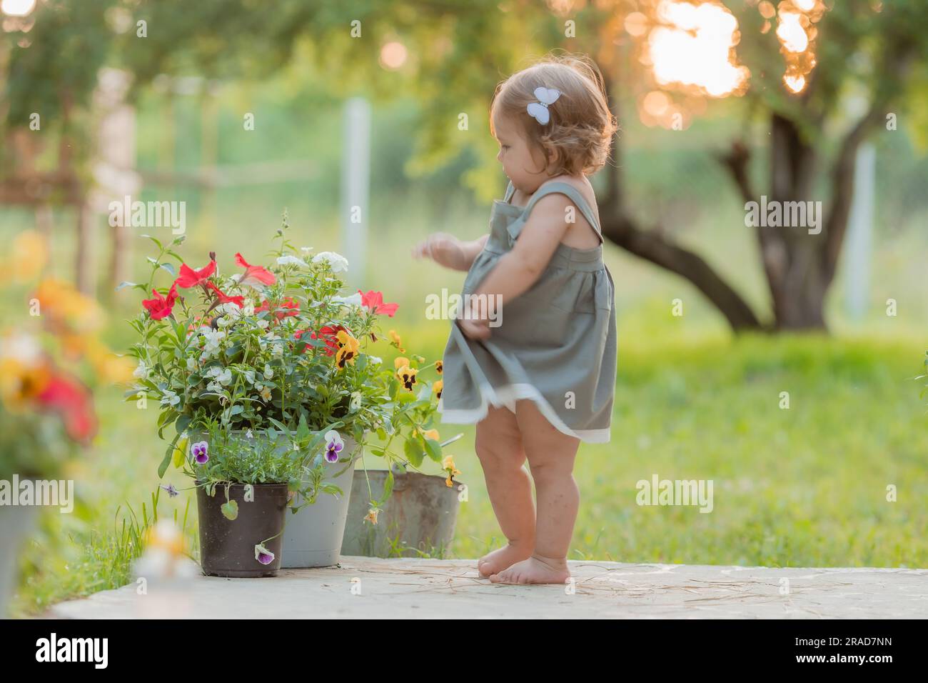 una graziosa bambina con un abito da sole in cotone verde cammina in estate al tramonto in estate a piedi nudi al tramonto. Foto di alta qualità Foto Stock