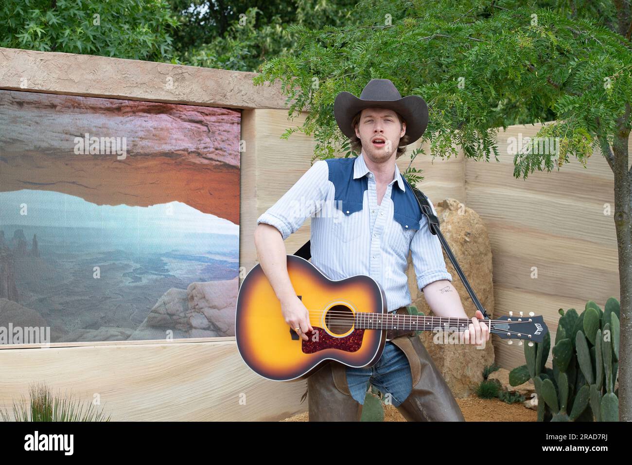 East Molesey, Surrey, Regno Unito. 3 luglio 2023. Membro del cast del pluripremiato musical del West End "Oklahoma" che esegue la canzone di successo dello spettacolo passeggiando nel deserto e nella foresta del giardino, E paesaggi di prateria in questo tributo tutto americano alla vigilia della famosa festa degli Stati Uniti, il 4 luglio/Independence Day in the America's Wild, presentato da Trailfinders e visita lo USA Show Garden. Era una bella mattinata di sole nei giardini dell'Hampton Court Palace per il RHS Hampton Court Palace Garden Festival Press Day. Credito: Maureen McLean/Alamy Live News Foto Stock