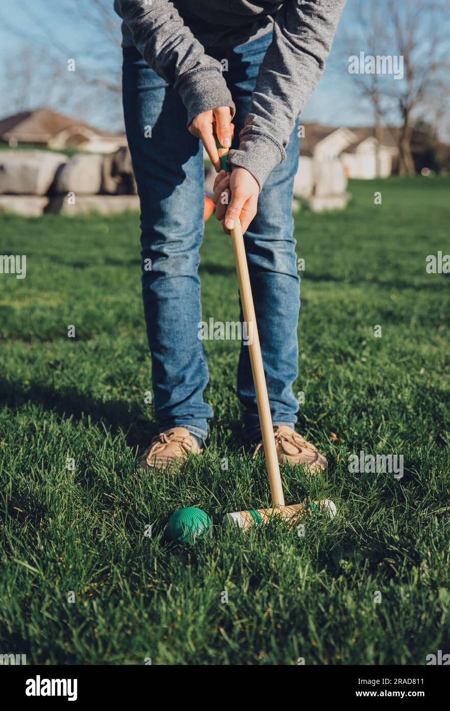 Immagine ritagliata di un adolescente che colpisce la palla da croquet con un mazzuolo. Foto Stock