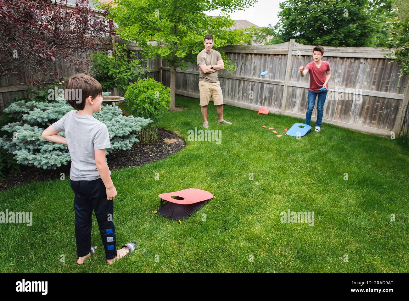 Due ragazzi che giocano alla partita di corn hole nel cortile con papà che li guarda. Foto Stock