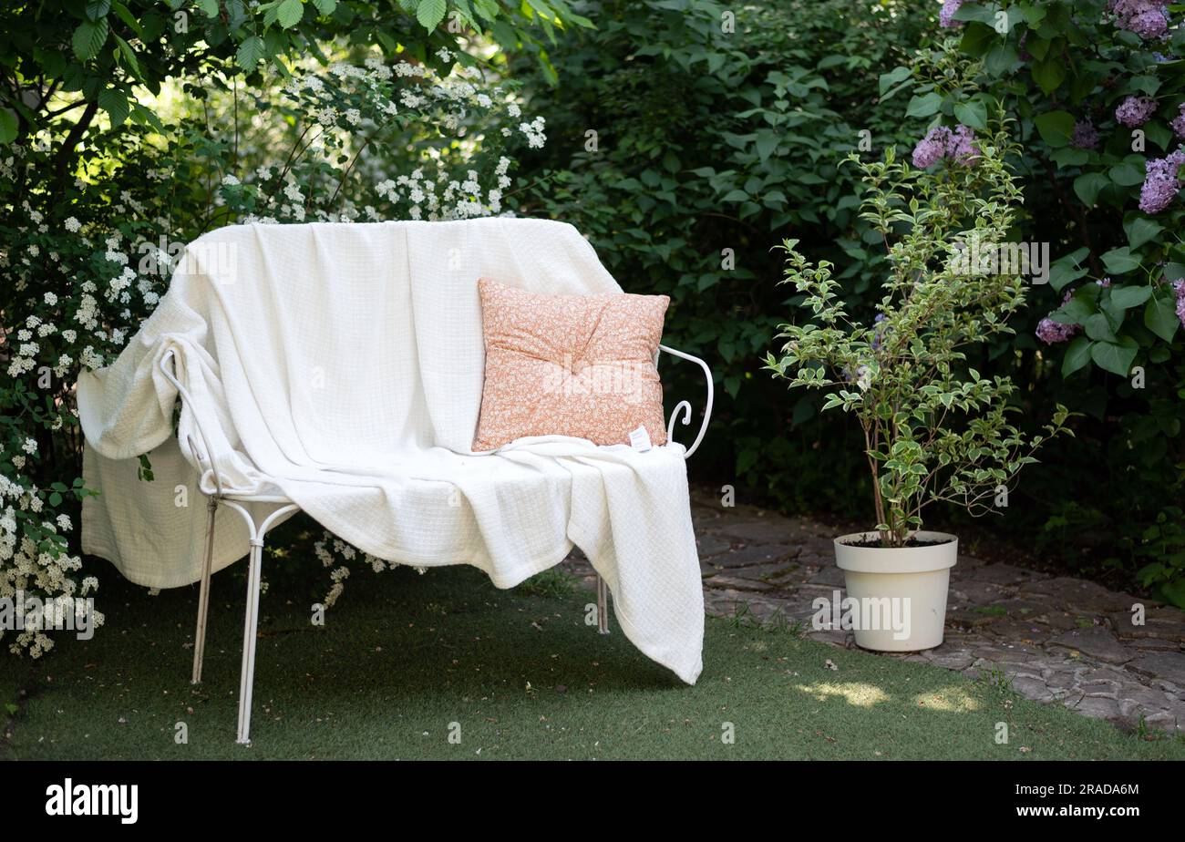 panca in metallo bianco forgiato in giardino con coperta e cuscino Foto Stock