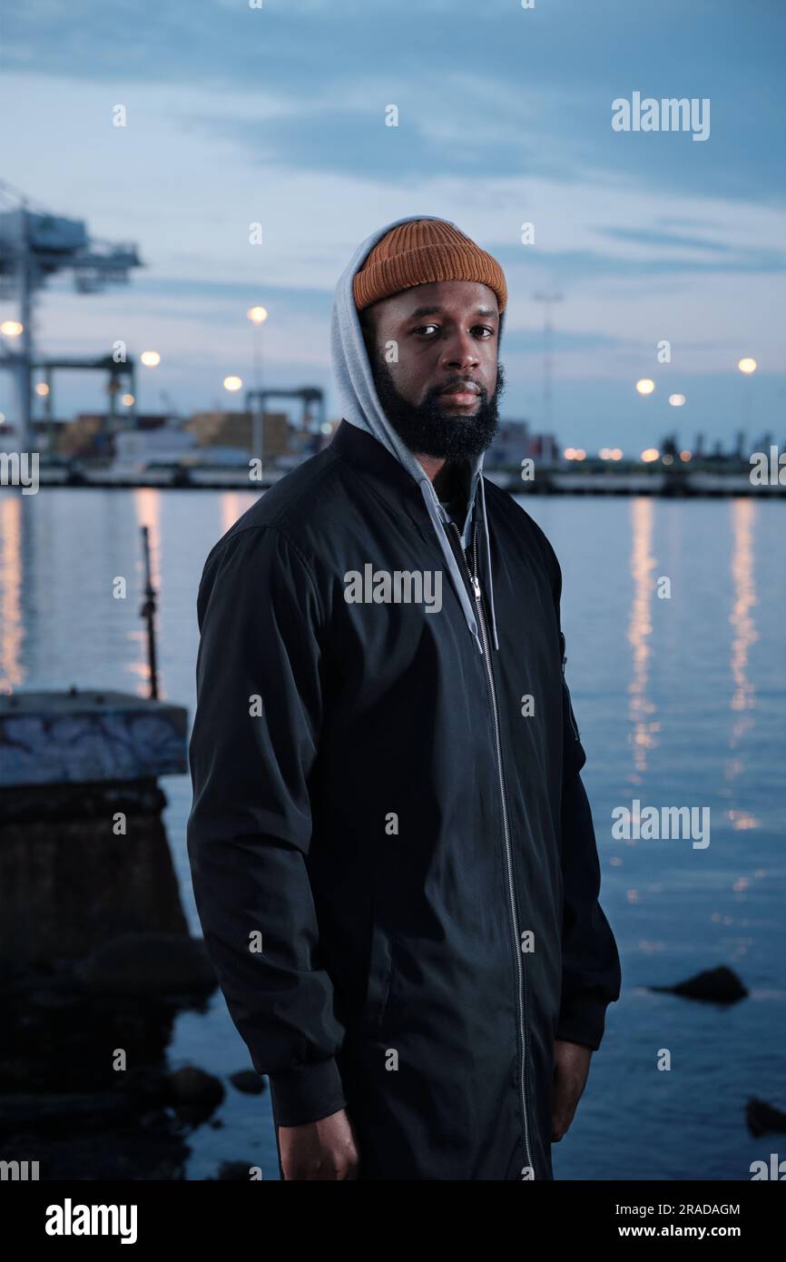 Solitudine: Uomo afro-americano in piedi da solo vicino a un canale di notte Foto Stock