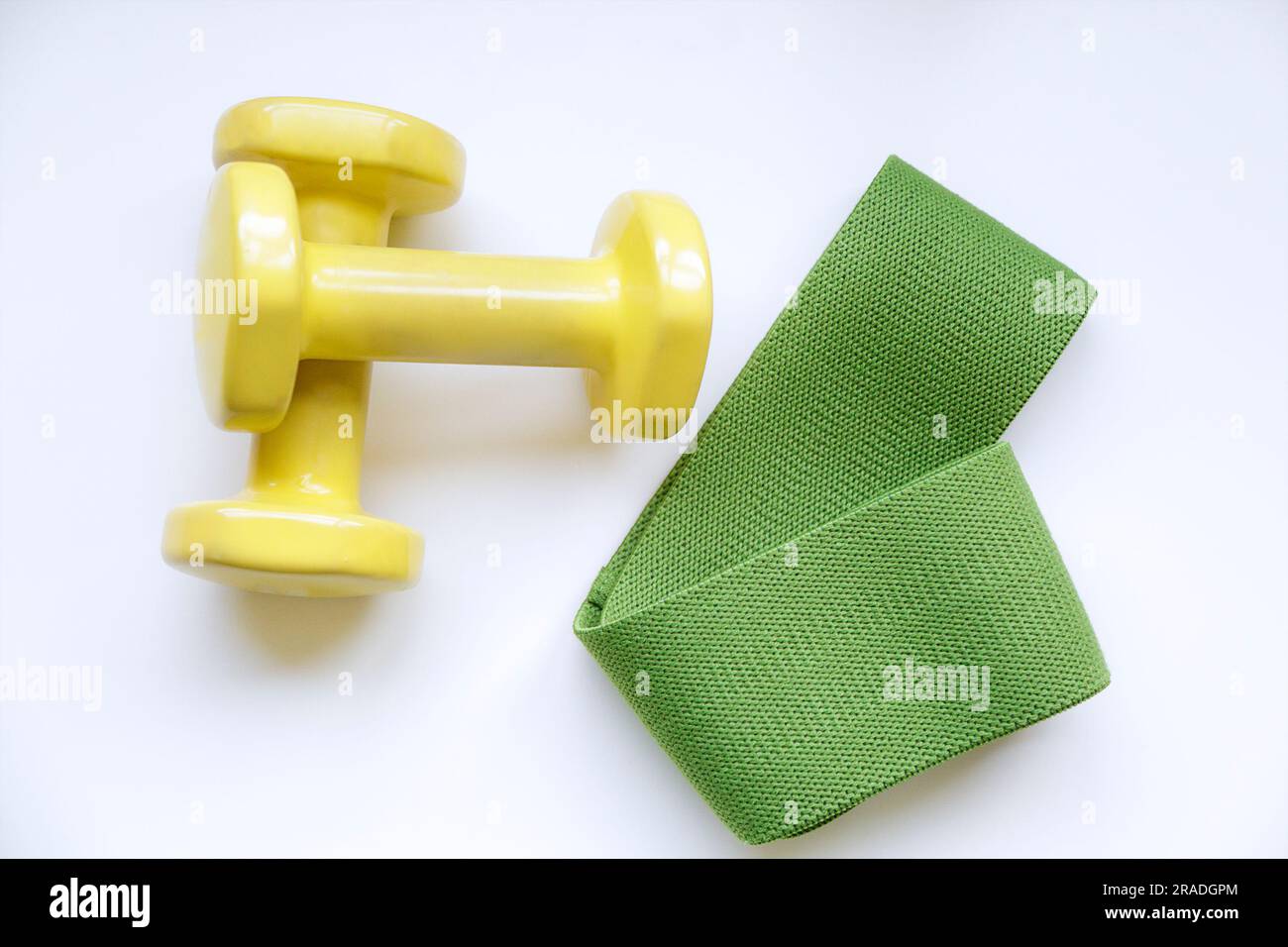 Attrezzature sportive. Un paio di manubri gialli e una fascia elastica verde per il fitness. Foto Stock