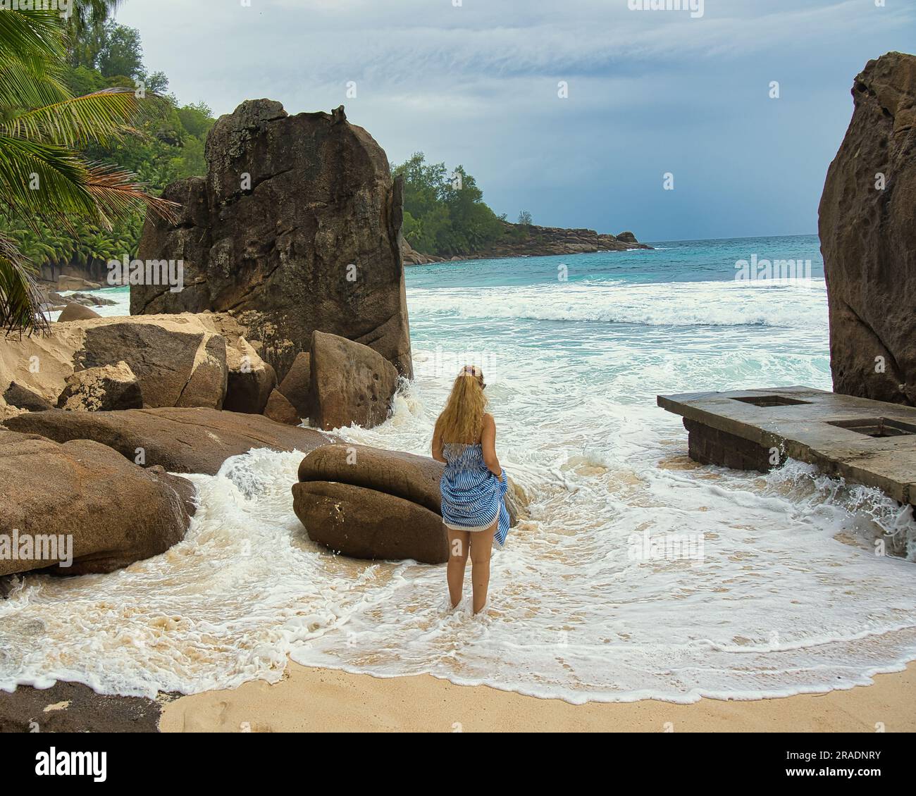 Bellissimi massi di roccia e spiaggia di sabbia bianca di intendance, donna di mezza età in piedi tra le rocce e le onde, Mahe Seychelles Foto Stock