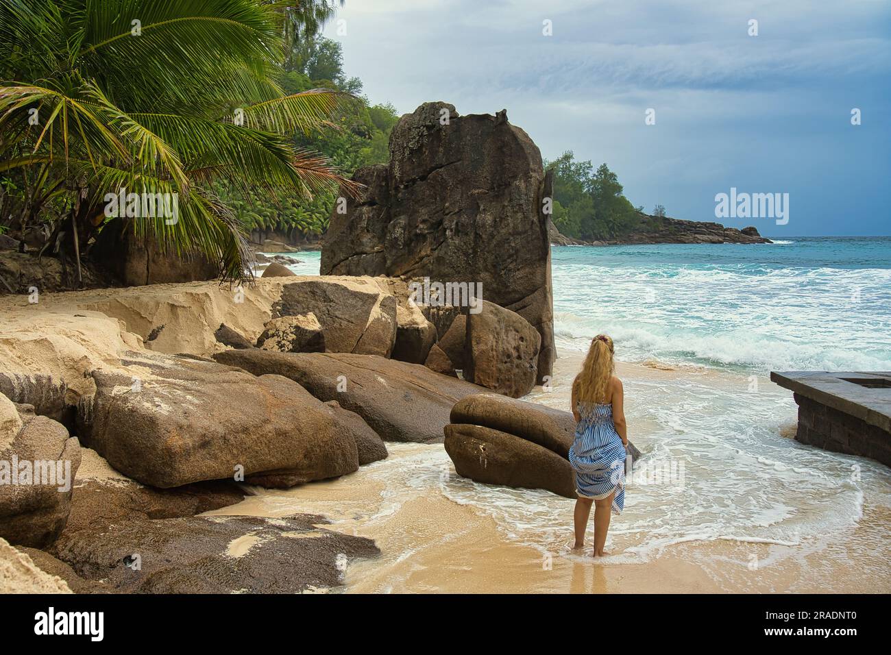 Bellissimi massi di roccia e spiaggia di sabbia bianca di intendance, donna di mezza età in piedi tra le rocce e le onde, Mahe Seychelles Foto Stock