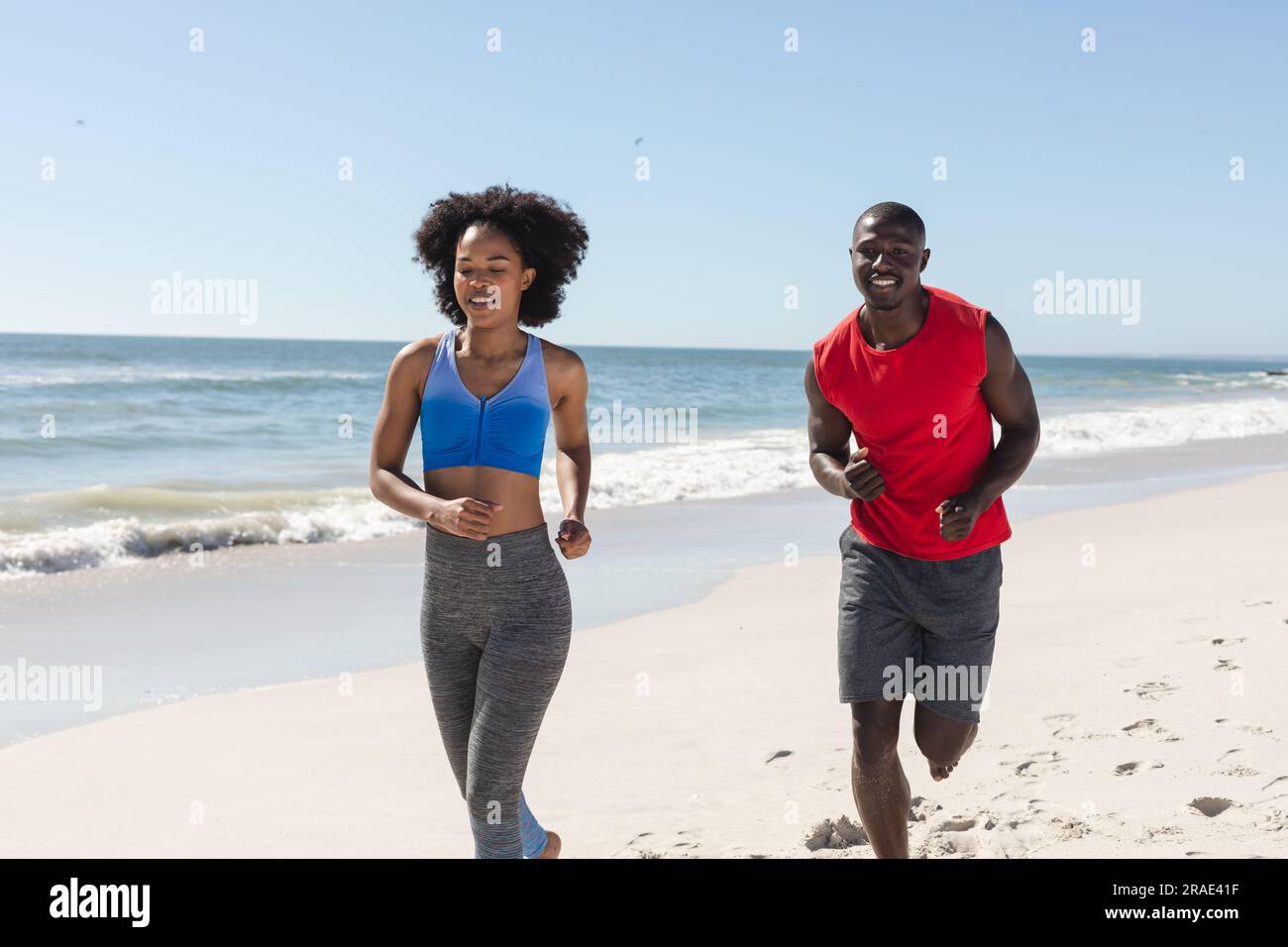 Una coppia afroamericana in forma e felice, che corre su una spiaggia soleggiata Foto Stock